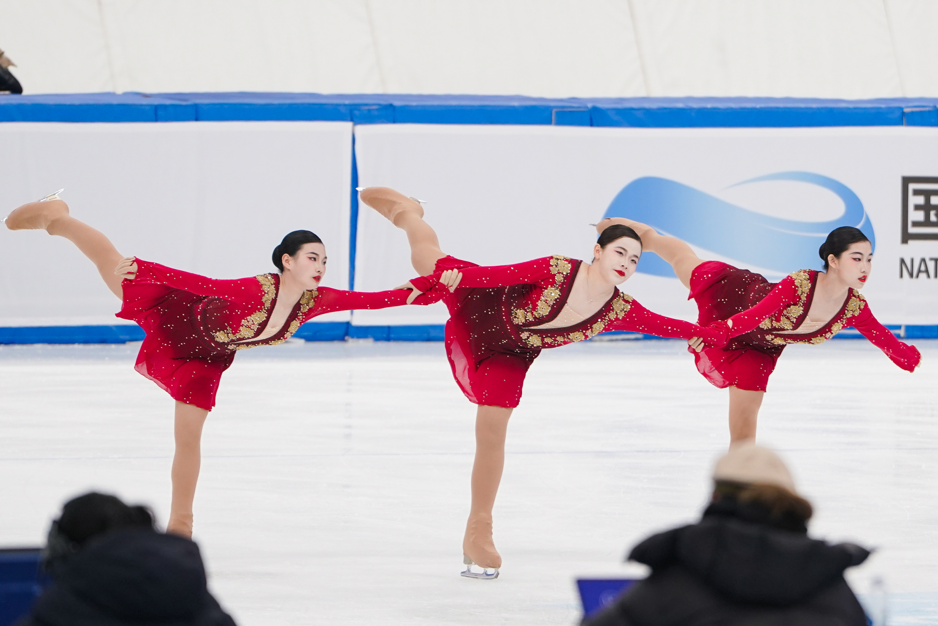 Three figure skaters in red costumes performing together